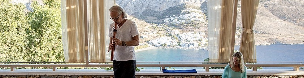 An elder man playing flute standing beside a woman